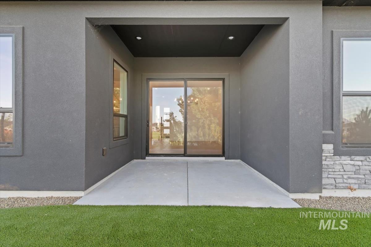 Property entrance with stone siding, stucco siding, and a patio area
