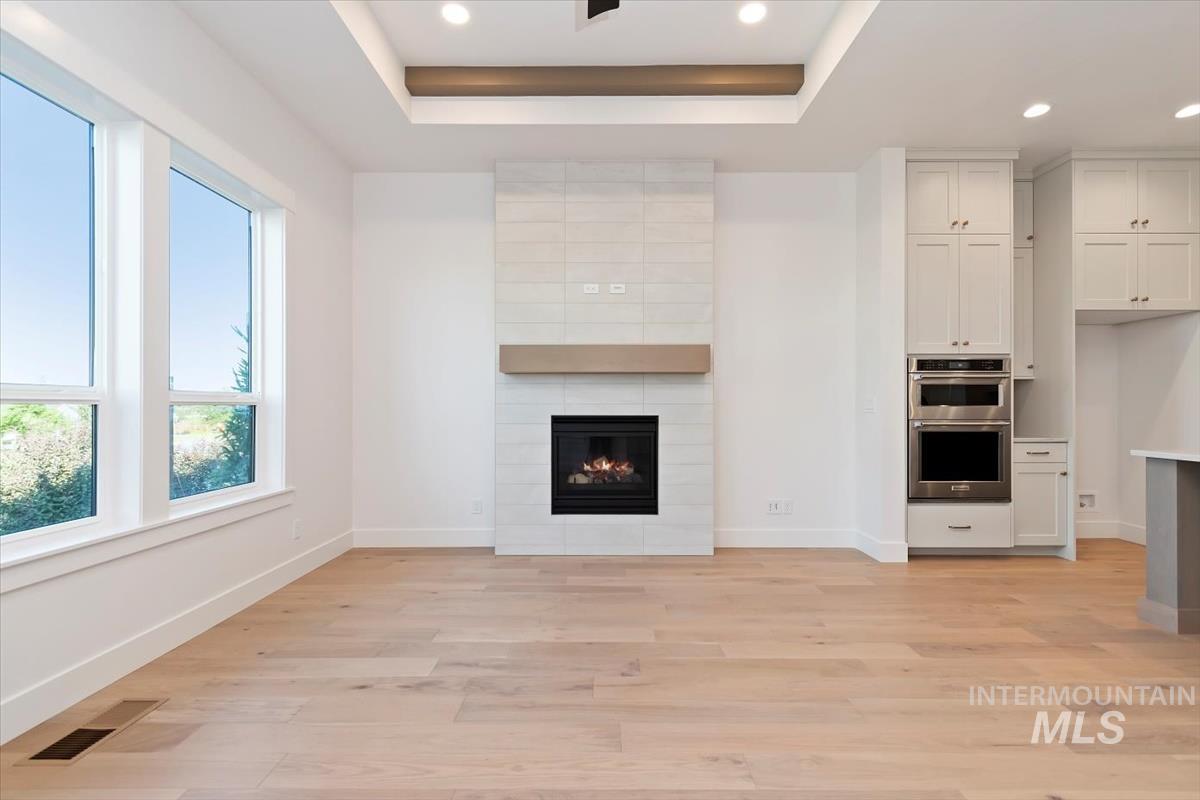 Unfurnished living room with a raised ceiling, a large fireplace, light wood-style floors, and recessed lighting