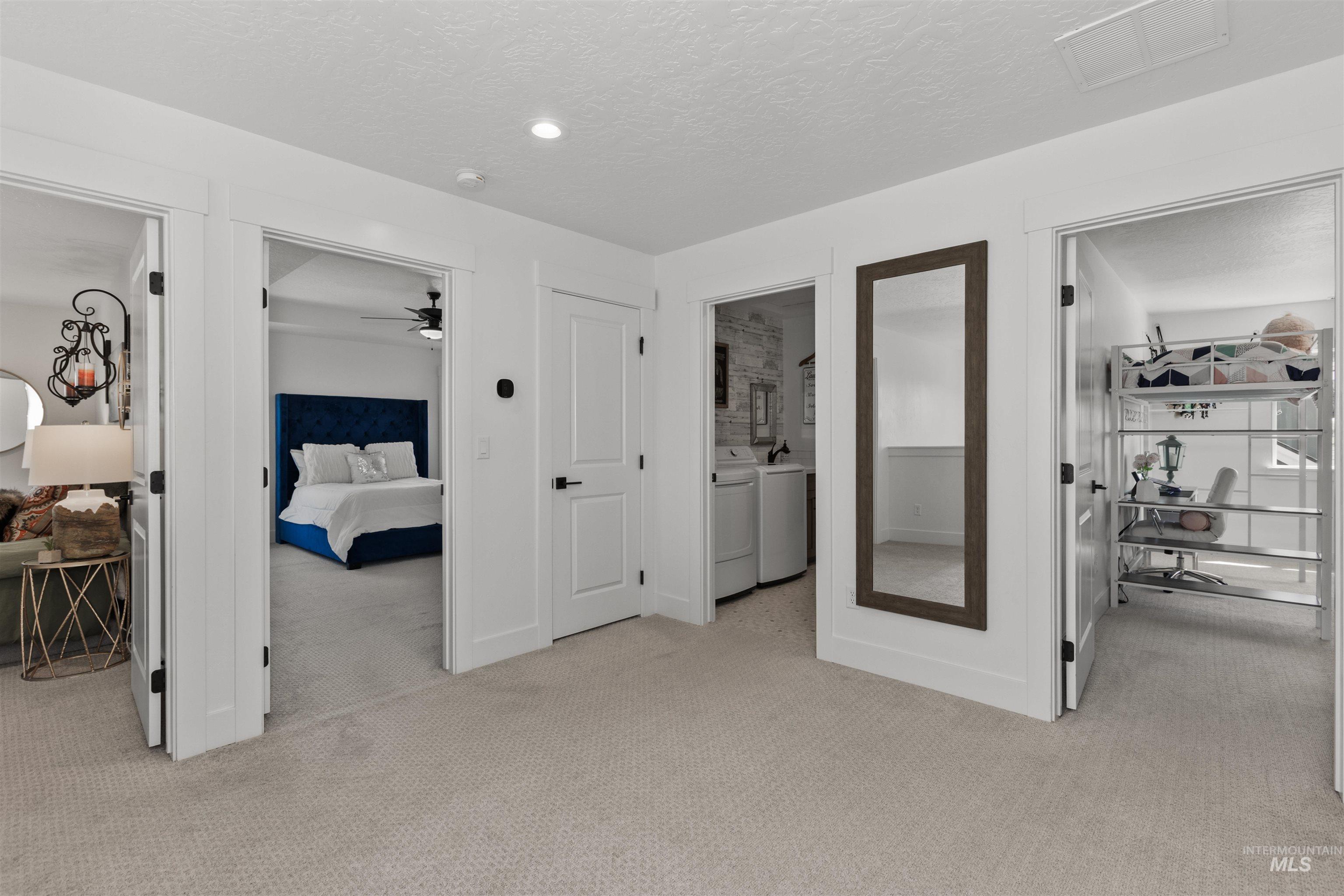 Bedroom featuring light carpet, a textured ceiling, washer and dryer, and ensuite bath