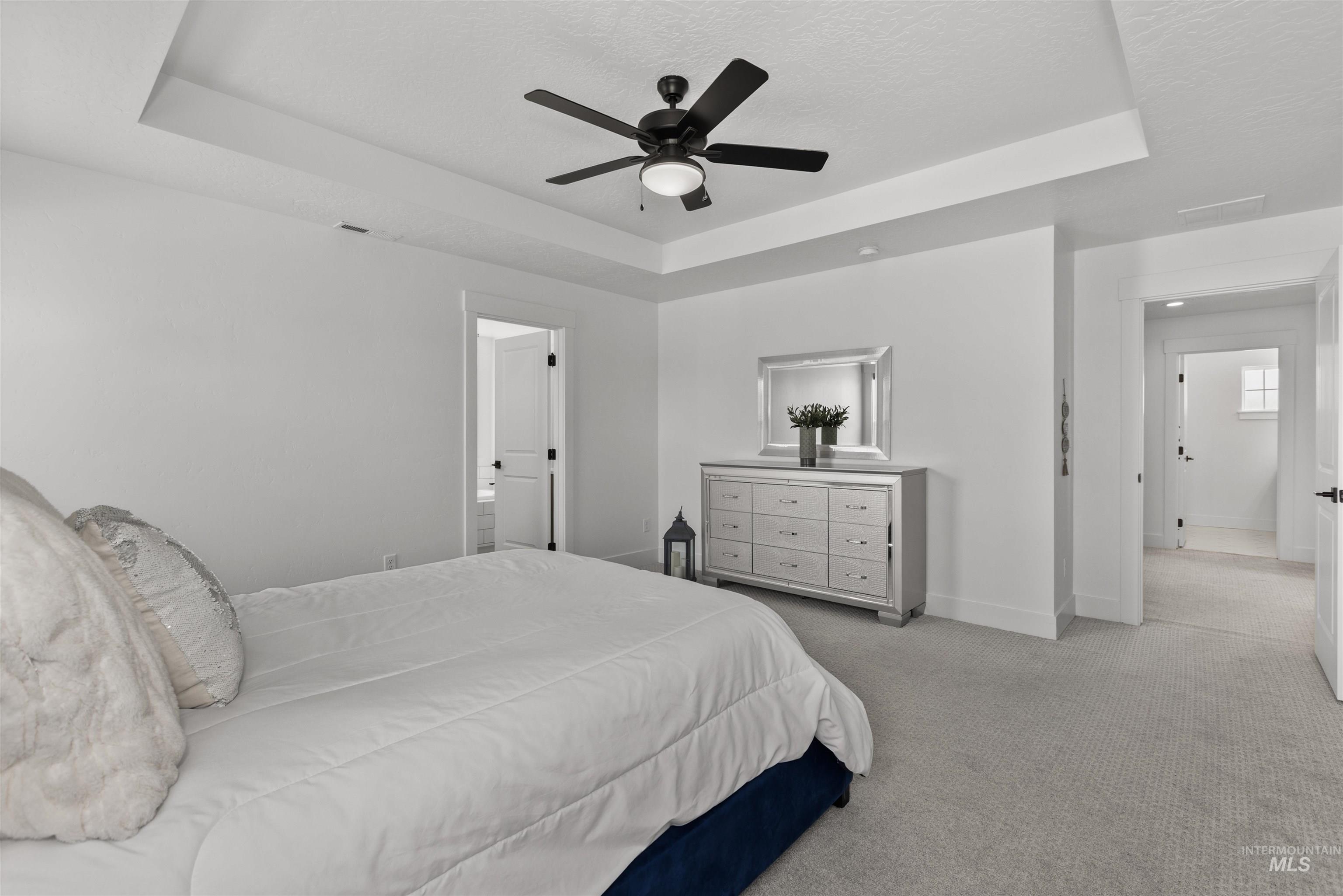 Bedroom featuring a raised ceiling, light carpet, ceiling fan, and a textured ceiling