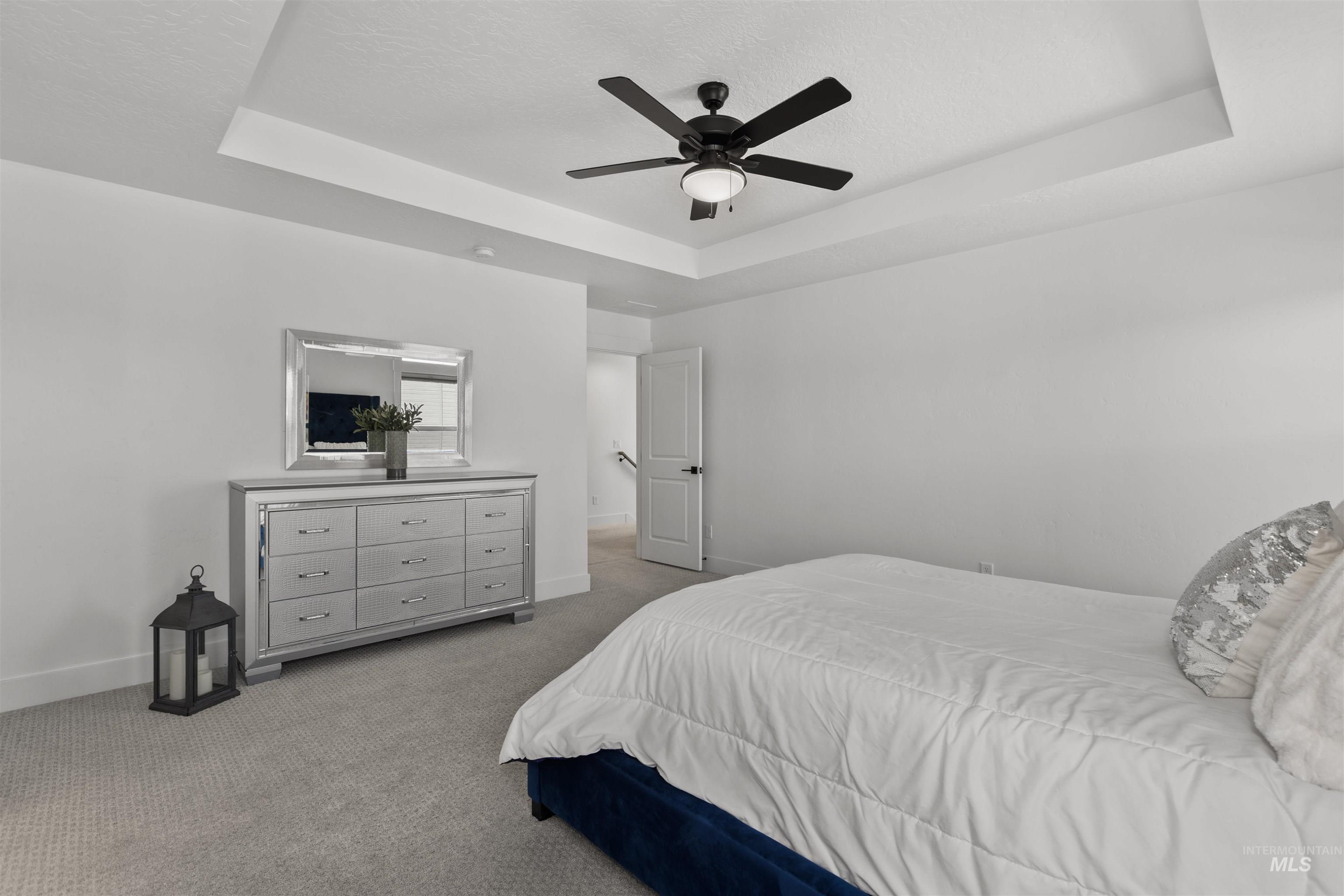 Carpeted bedroom featuring a raised ceiling, a ceiling fan, and a textured ceiling