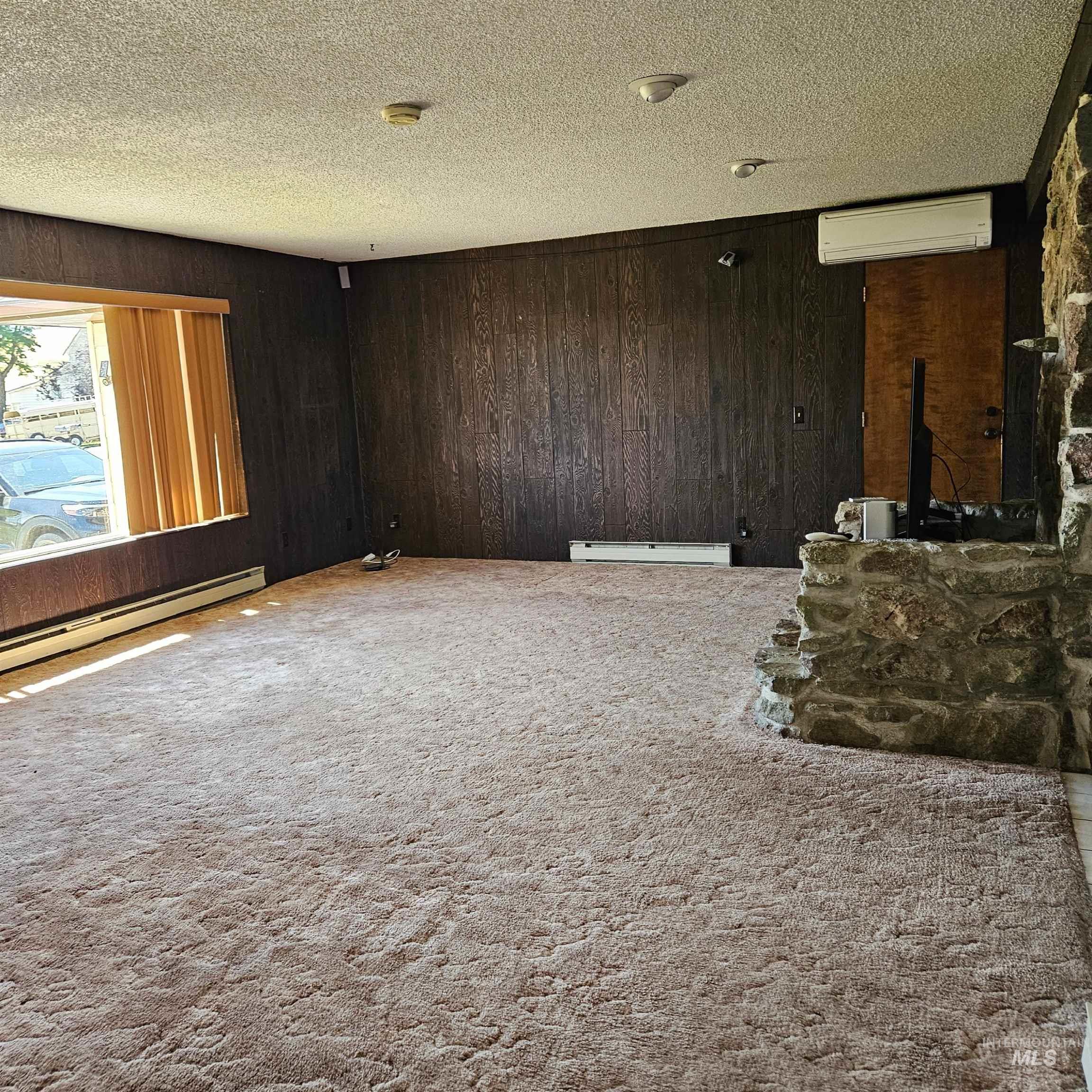 Unfurnished living room with wooden walls, carpet flooring, a textured ceiling, a wall mounted air conditioner, and baseboard heating