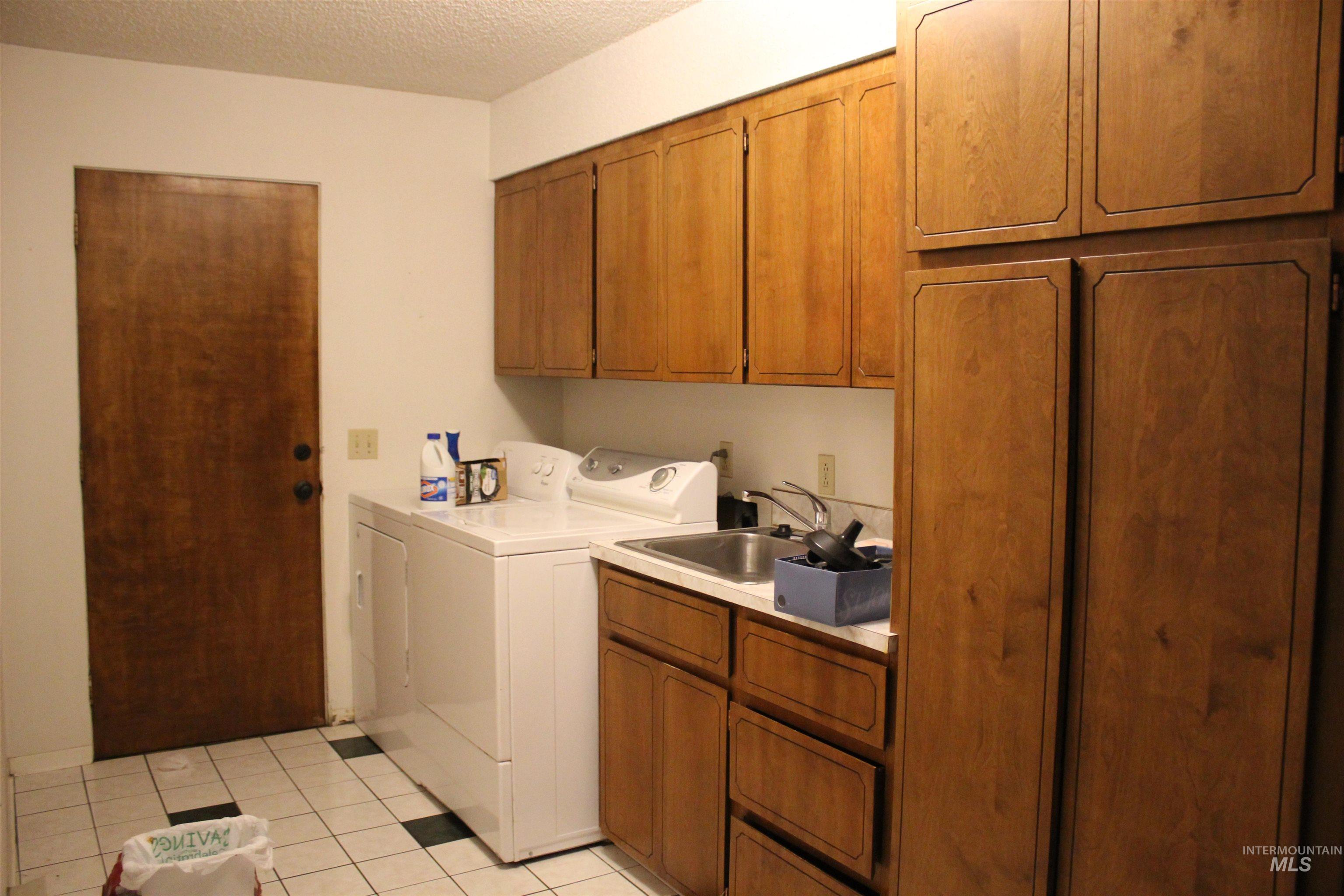 Laundry area featuring cabinet space, washer and clothes dryer, light tile patterned floors, and a textured ceiling
