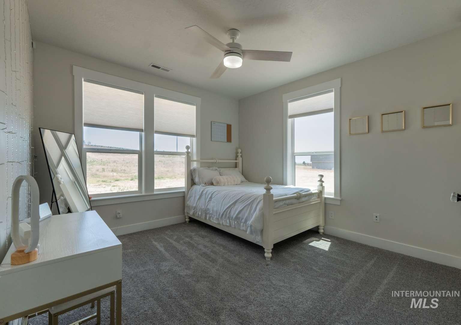 Bedroom with multiple windows, dark colored carpet, and a ceiling fan