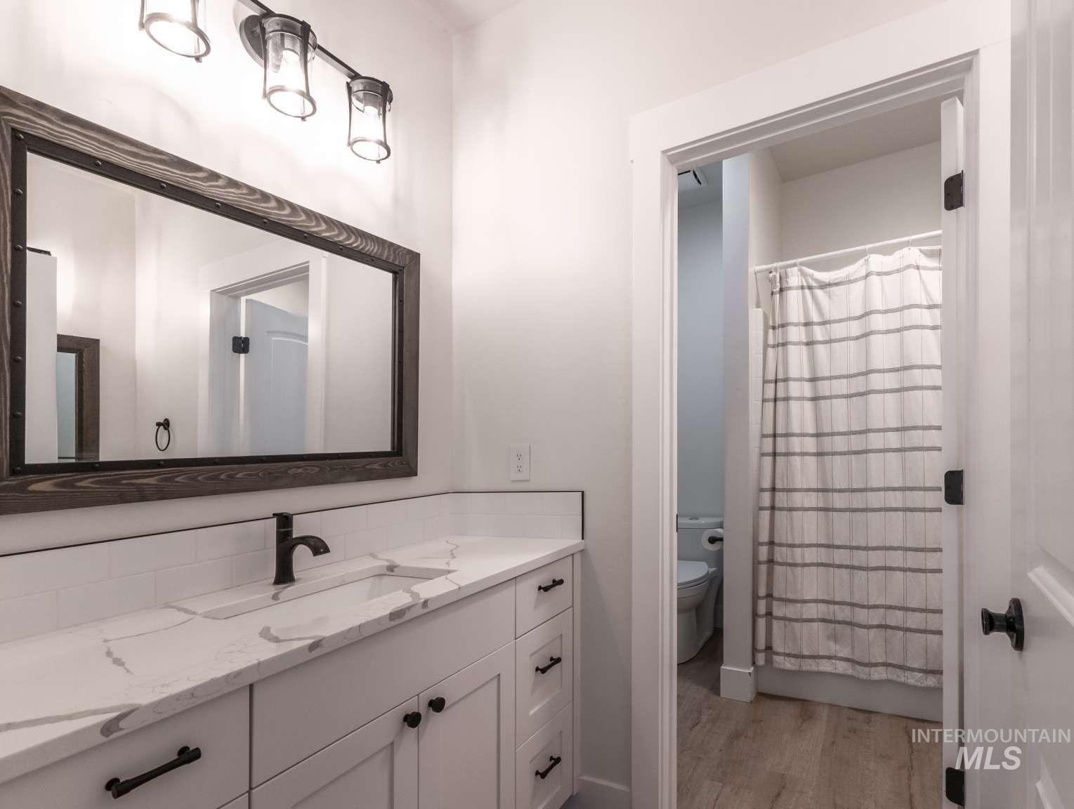 Full bathroom with vanity, a shower with shower curtain, tasteful backsplash, and light wood finished floors