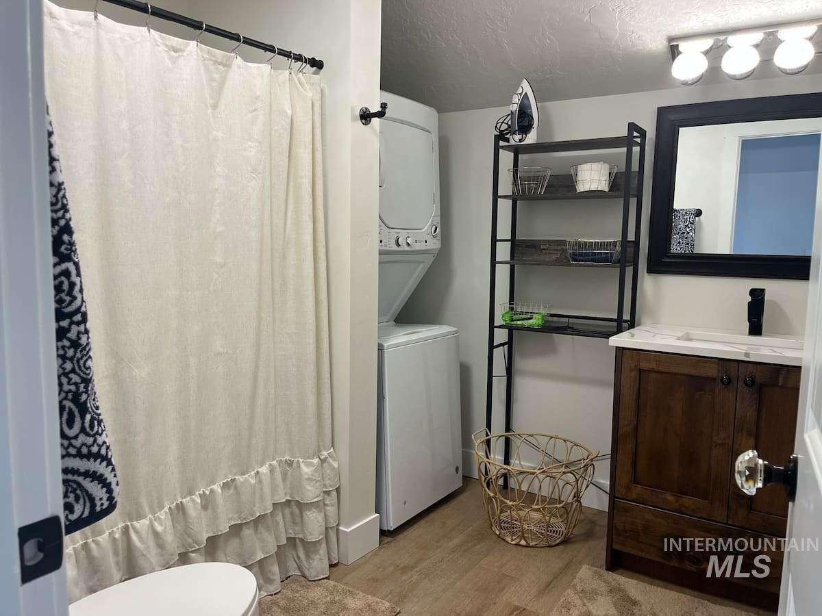 Bathroom featuring a shower with curtain, vanity, a textured ceiling, light wood-style flooring, and stacked washer / drying machine