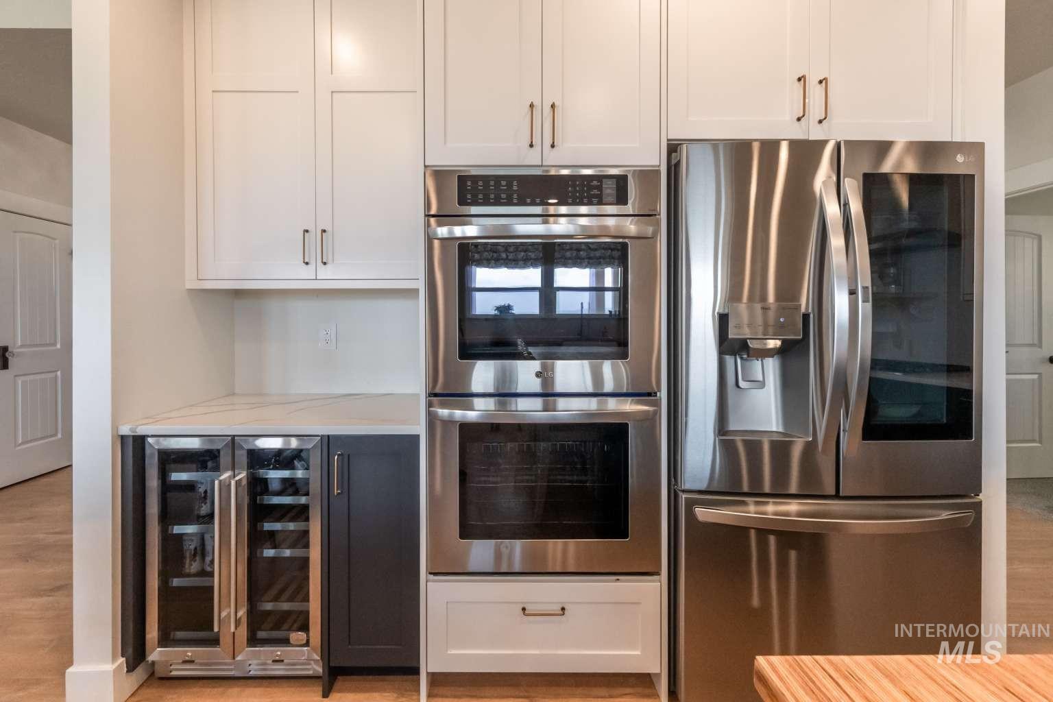 Kitchen featuring white cabinetry, appliances with stainless steel finishes, beverage cooler, light wood finished floors, and light stone counters