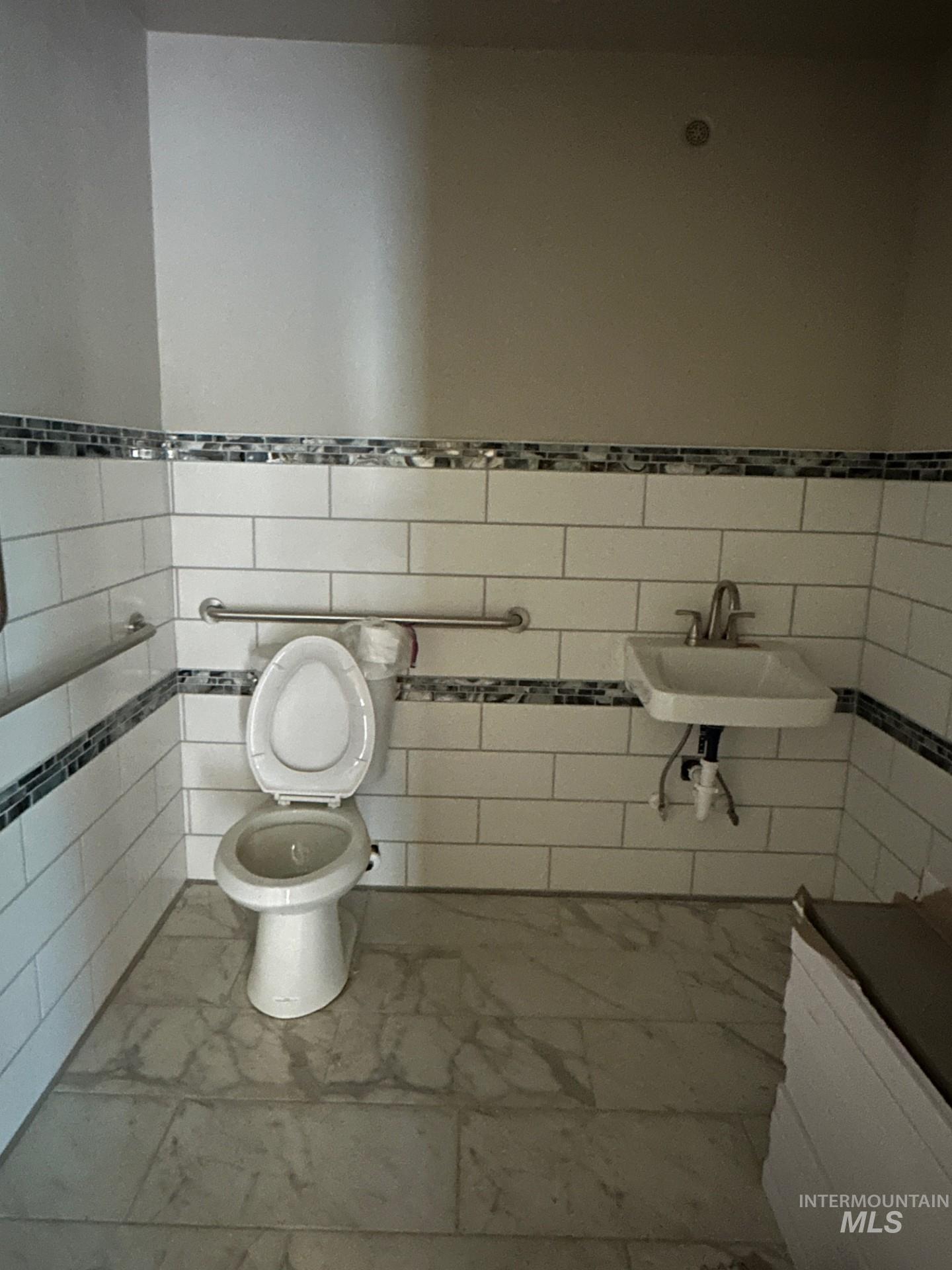 Half bath featuring marble finish floors, tile walls, and wainscoting