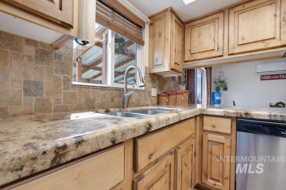 Kitchen featuring dishwasher, backsplash, light brown cabinets, a wall mounted AC, and light stone countertops