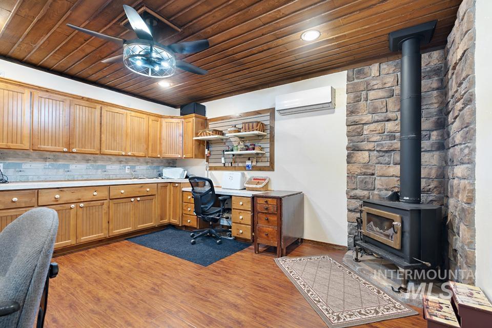 Home office with an AC wall unit, wood ceiling, a wood stove, a ceiling fan, and wood finished floors