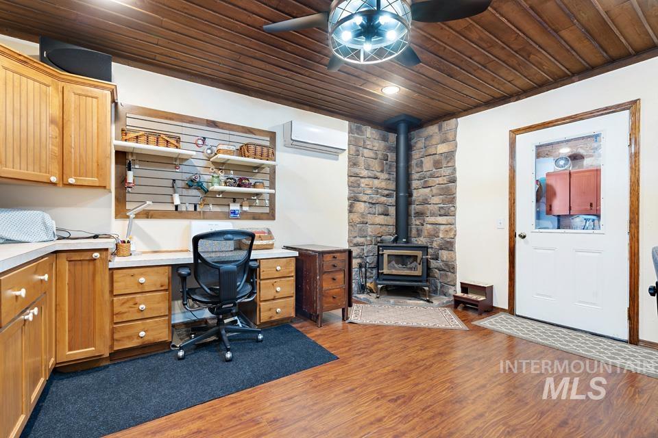 Office area with wood ceiling, ceiling fan, a wall mounted AC, dark wood-type flooring, and a wood stove