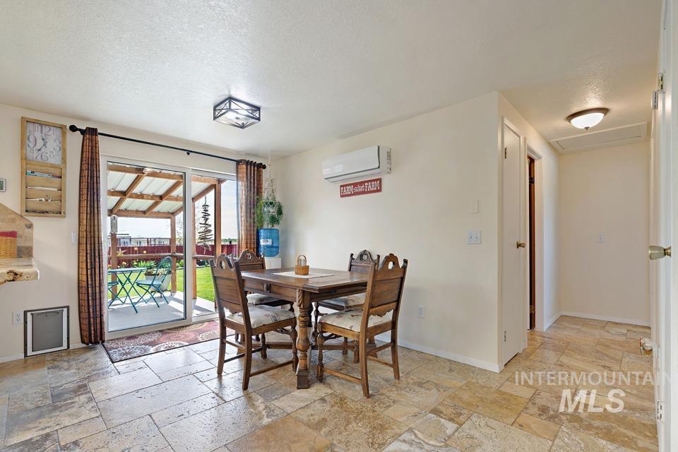 Dining space featuring stone tile flooring, a wall unit AC, and a textured ceiling