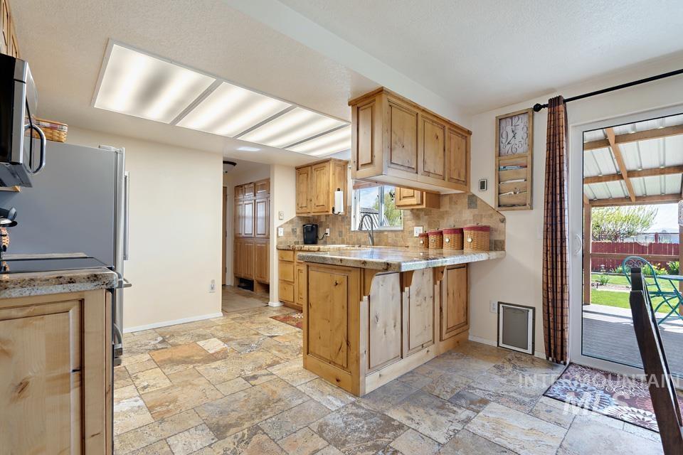 Kitchen featuring a peninsula, stone tile flooring, stainless steel microwave, and decorative backsplash