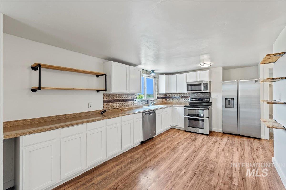 Kitchen with open shelves, appliances with stainless steel finishes, white cabinetry, and decorative backsplash