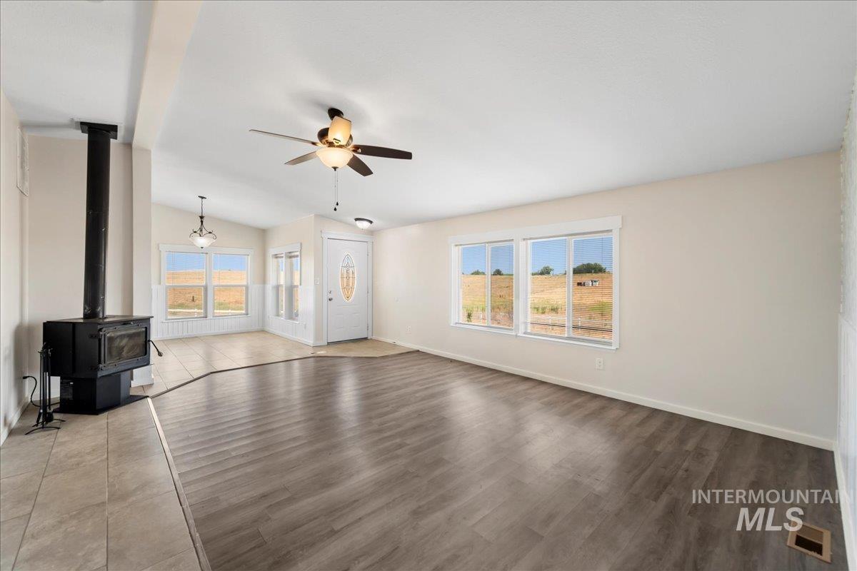 Unfurnished living room featuring ceiling fan, lofted ceiling, and a wood stove