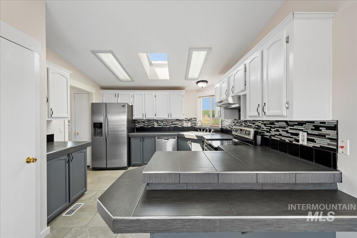 Kitchen with dark countertops, tasteful backsplash, white cabinetry, and stainless steel appliances