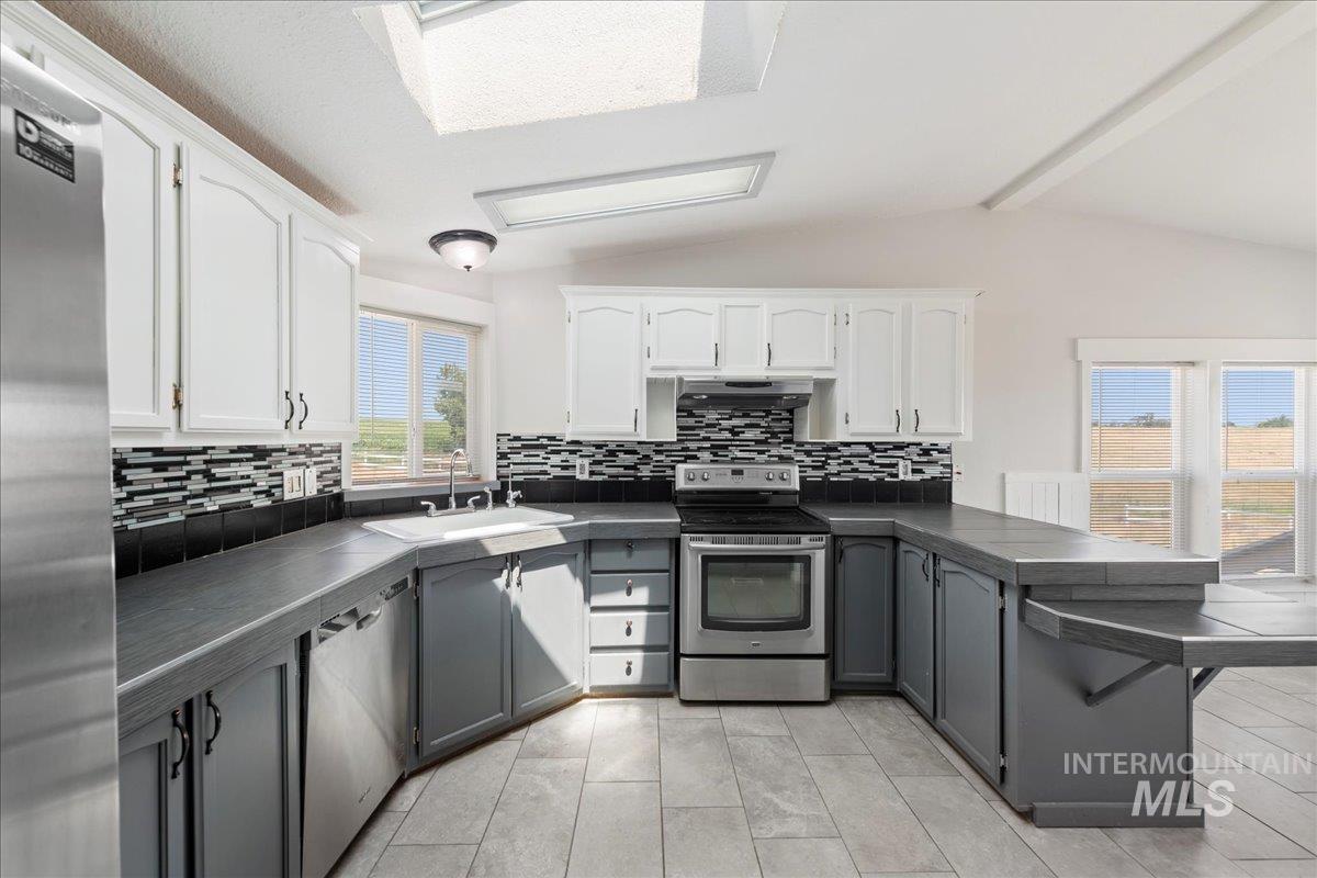 Kitchen featuring a peninsula, appliances with stainless steel finishes, backsplash, and white cabinets