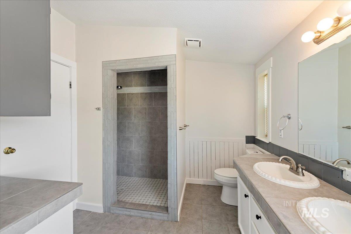 Bathroom featuring walk-in shower, double vanity, & tile floors.