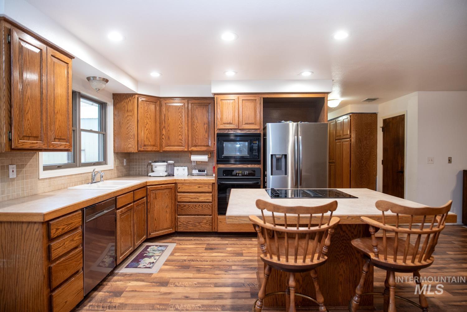 Kitchen featuring brown cabinets, dark wood finished floors, black appliances, tasteful backsplash, and a kitchen island