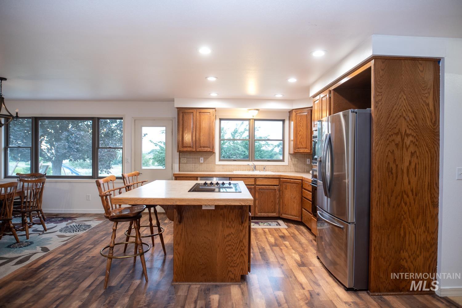 Kitchen with brown cabinets, light countertops, decorative backsplash, dark wood-style floors, and recessed lighting