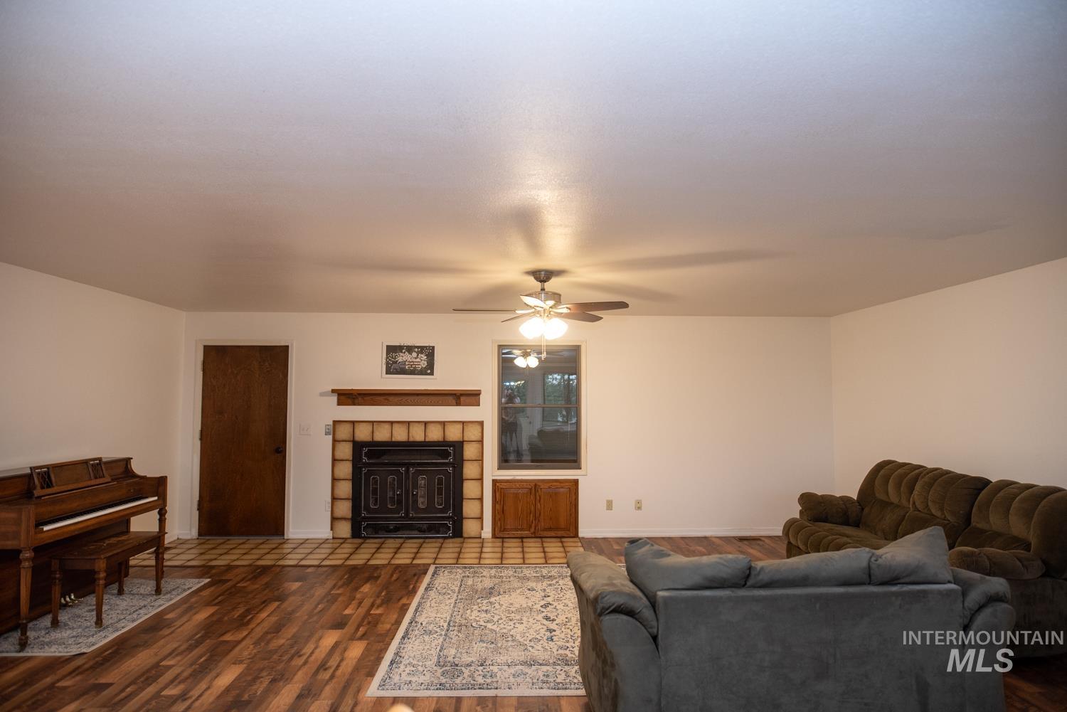 Living room featuring wood finished floors, ceiling fan, and a tiled fireplace