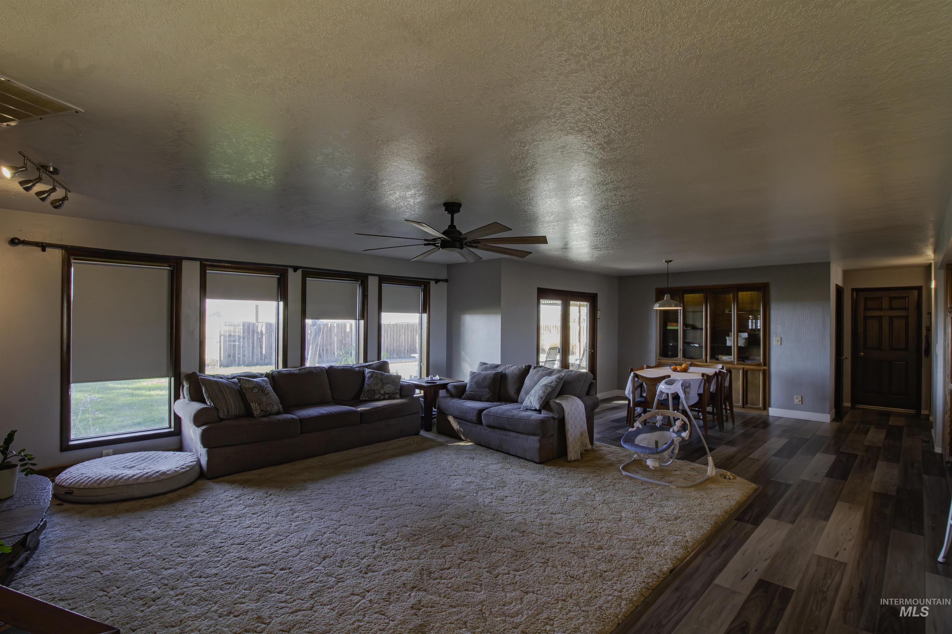 Living area with a textured ceiling, dark wood finished floors, ceiling fan, and healthy amount of natural light