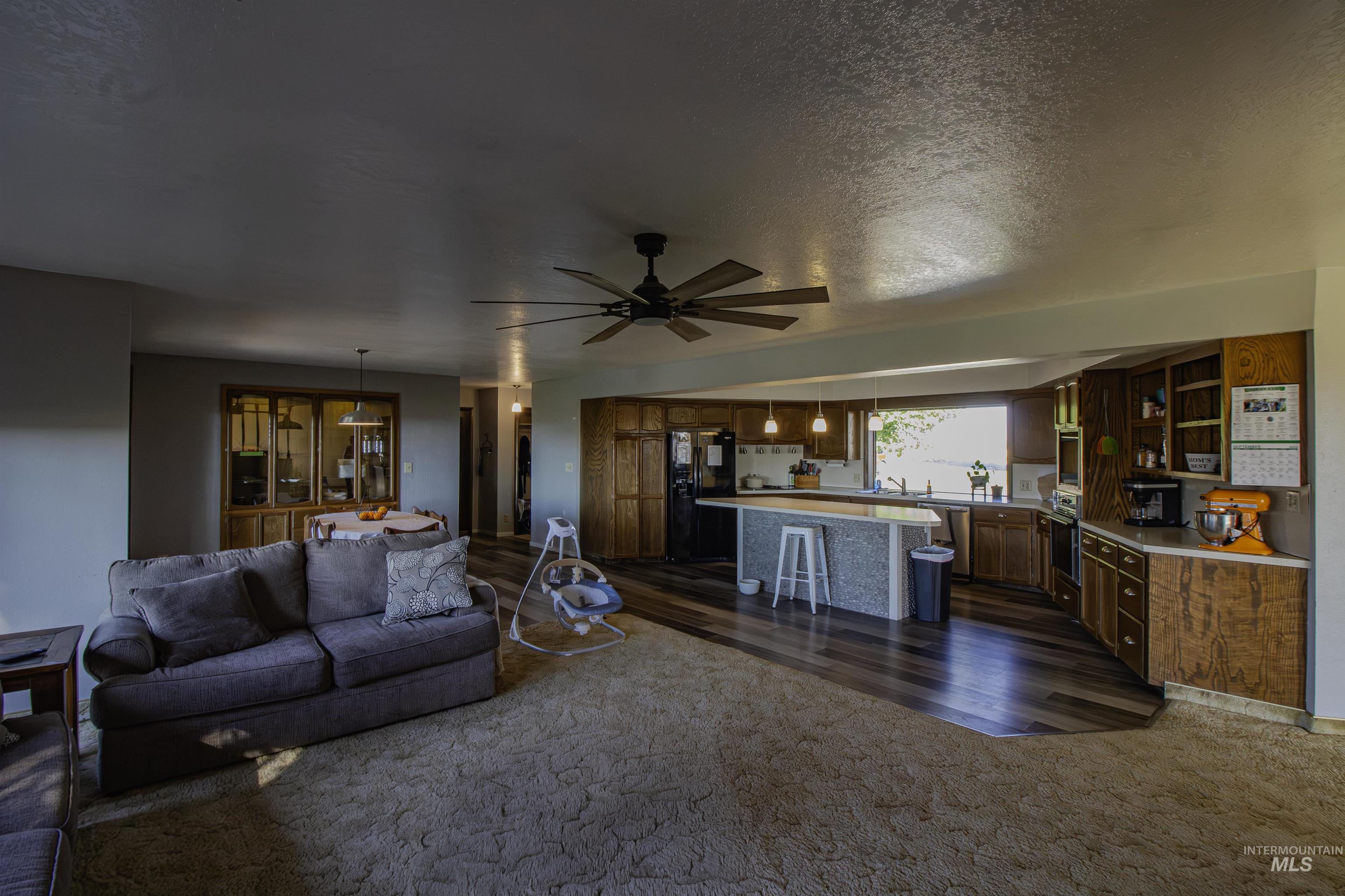 Living area featuring dark colored carpet, a textured ceiling, ceiling fan, and dark wood-style floors