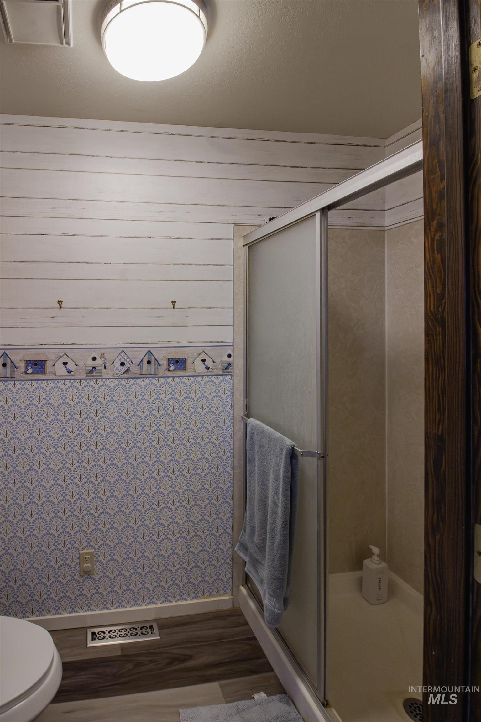 Bathroom featuring a stall shower, wood finished floors, and wooden walls