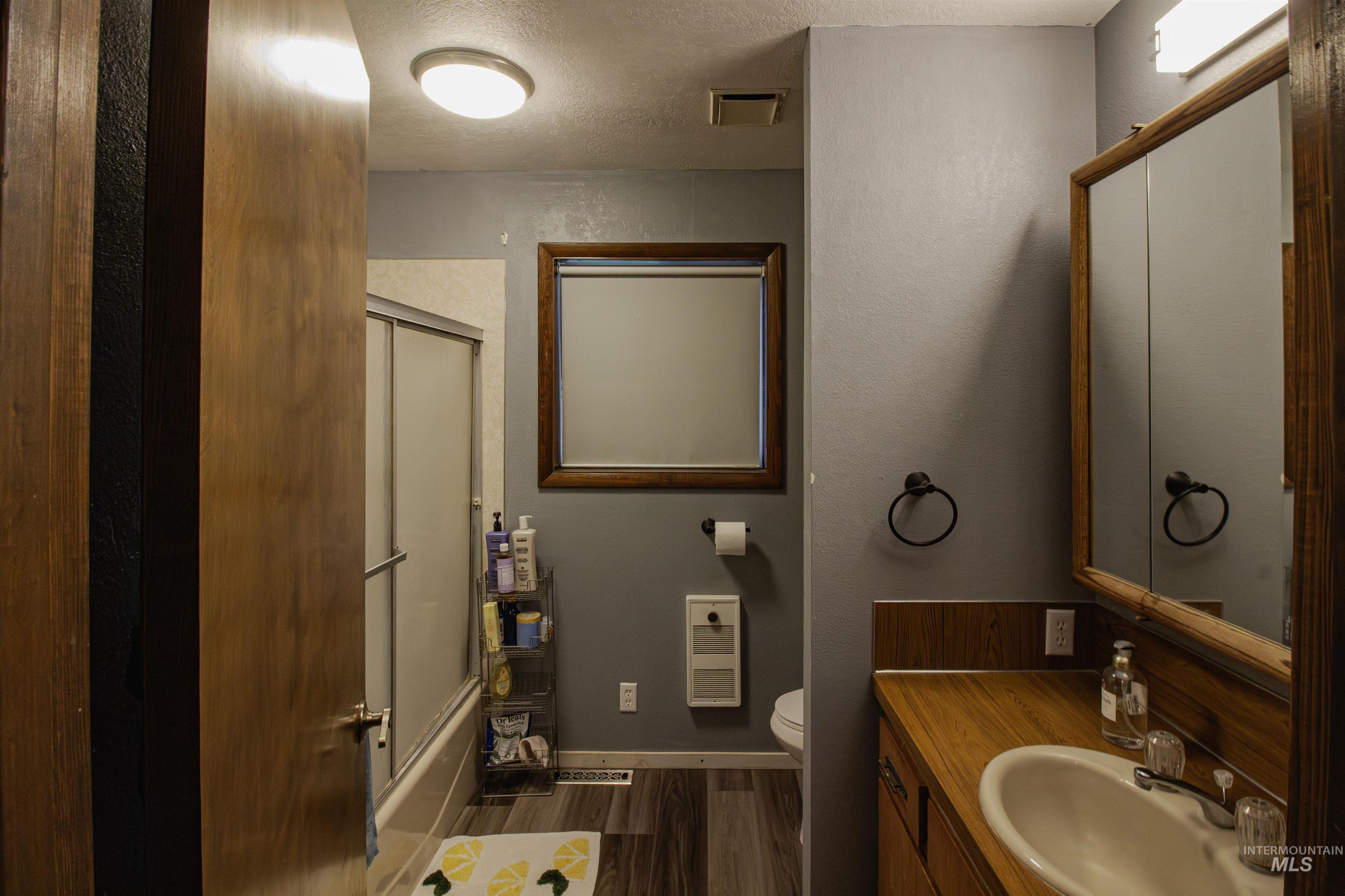 Full bath with bath / shower combo with glass door, dark wood-style floors, a textured ceiling, and vanity