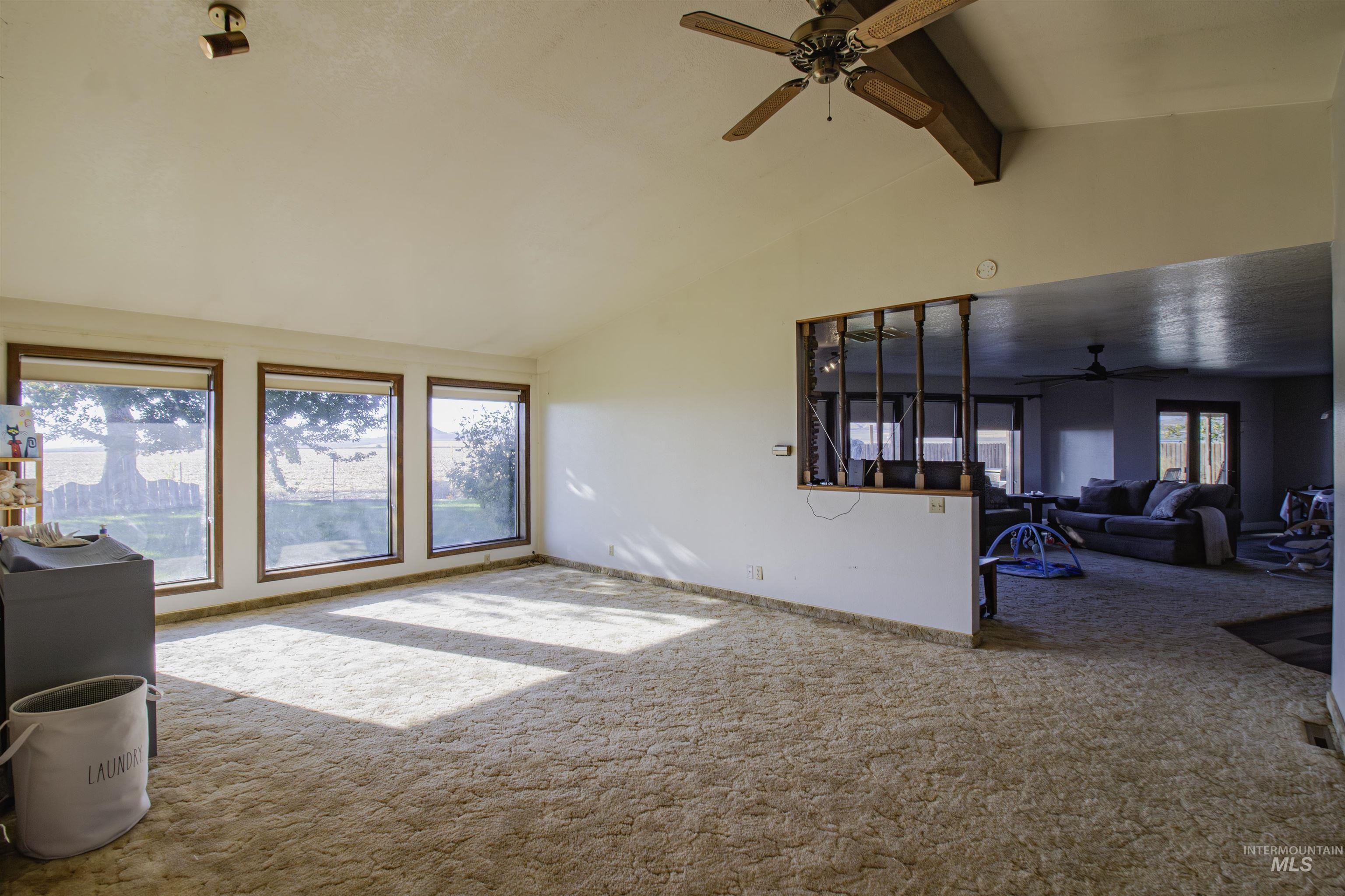 Carpeted living room with beamed ceiling, ceiling fan, and high vaulted ceiling