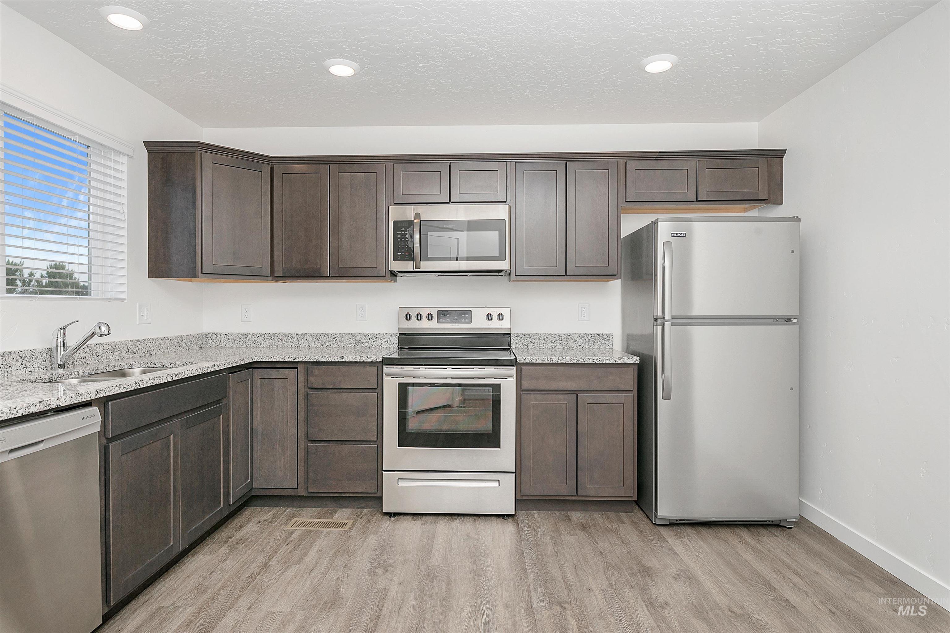 Kitchen with appliances with stainless steel finishes, dark brown cabinetry, light stone countertops, light wood-style floors, and a textured ceiling