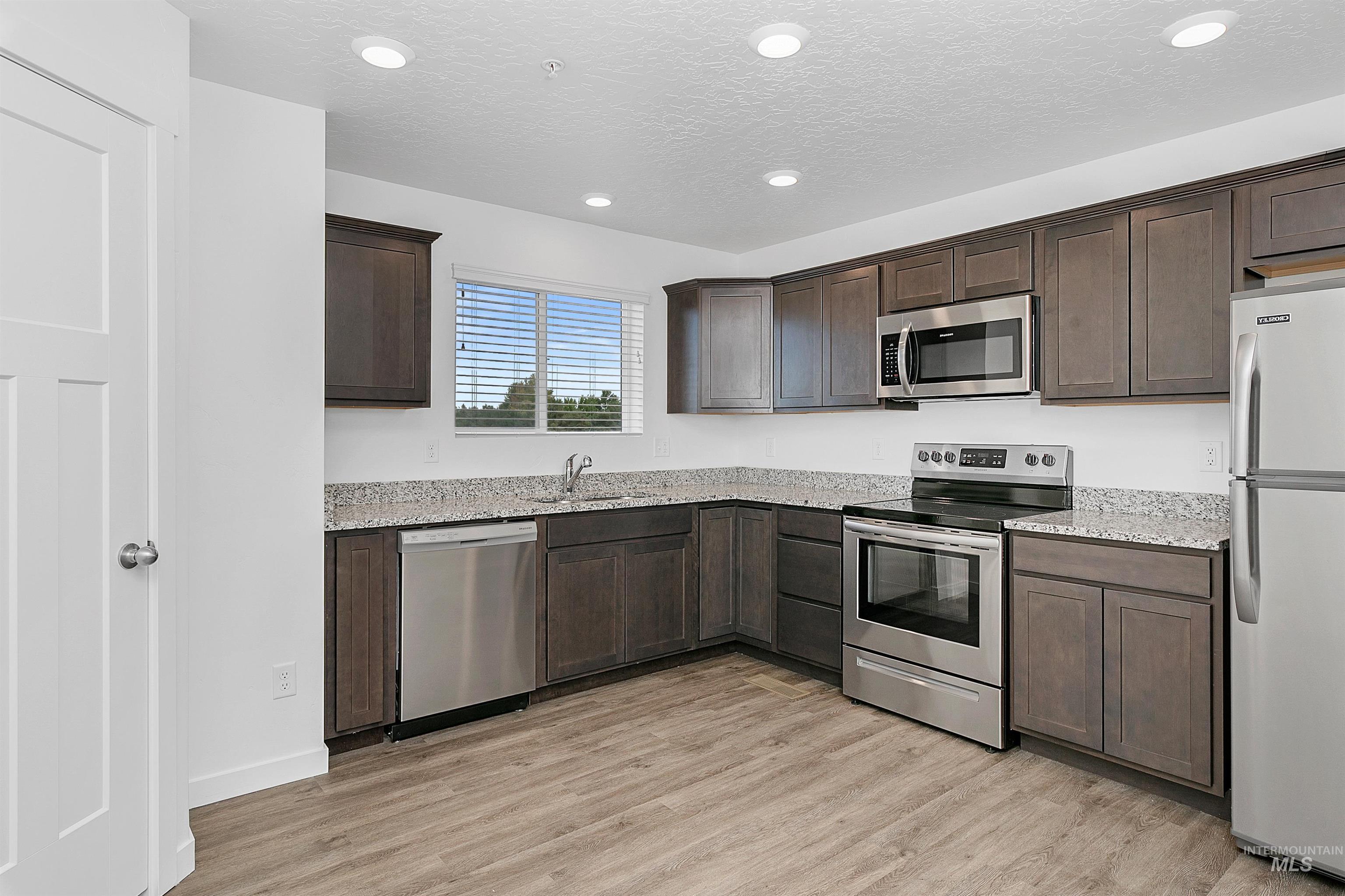 Kitchen with appliances with stainless steel finishes, dark brown cabinetry, light wood-style flooring, recessed lighting, and a textured ceiling