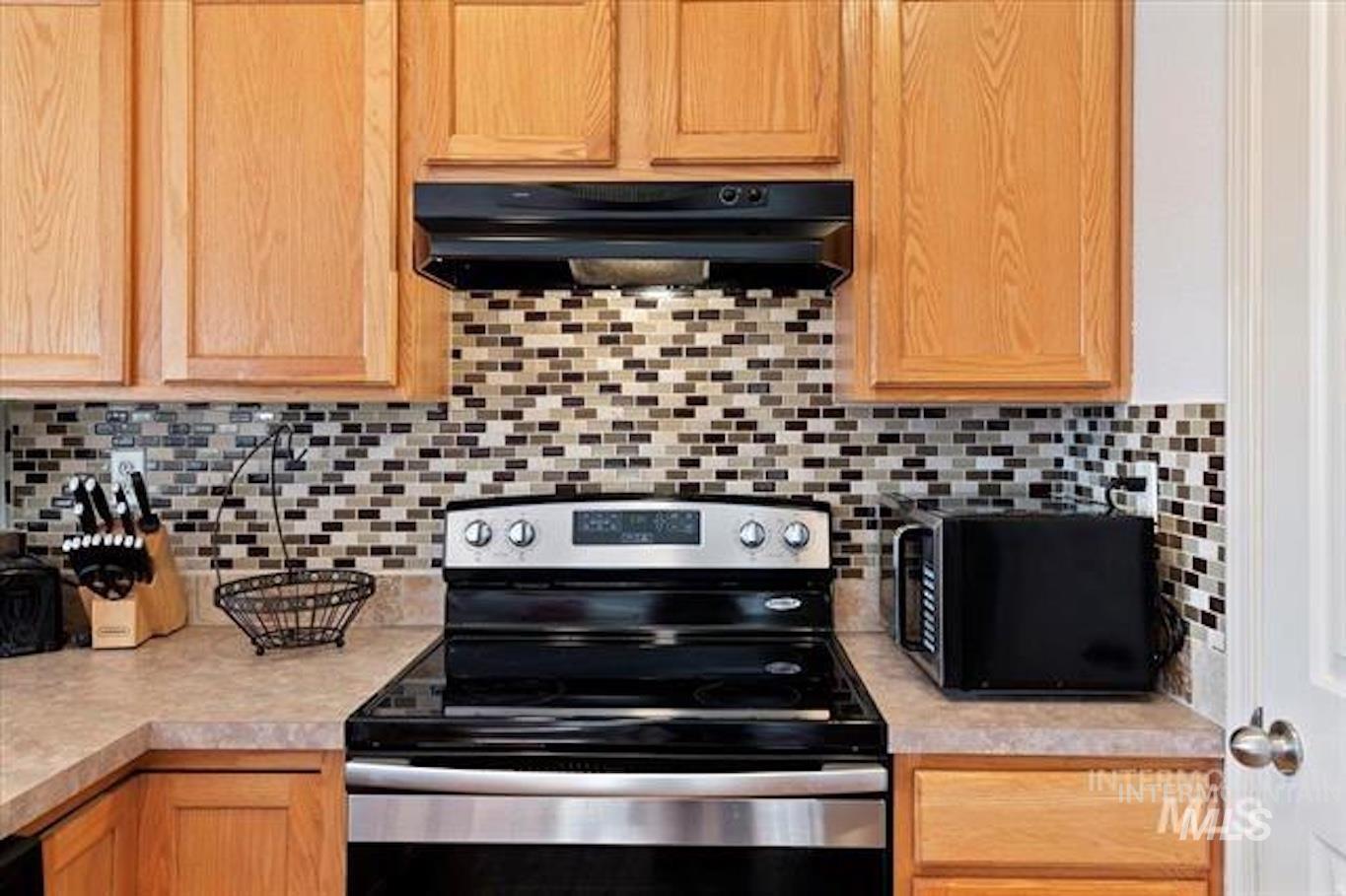 Kitchen featuring stainless steel electric stove, decorative backsplash, light countertops, black microwave, and under cabinet range hood