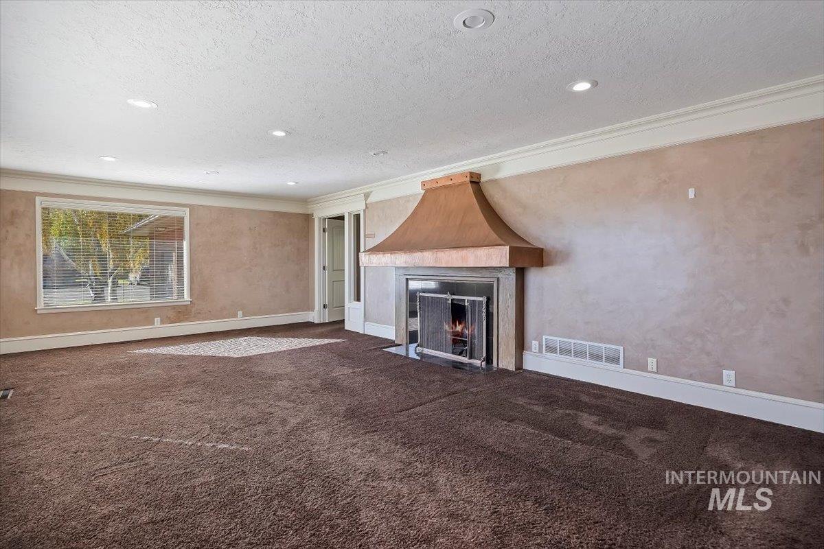 Unfurnished living room featuring crown molding, a fireplace, a textured ceiling, dark colored carpet, and recessed lighting