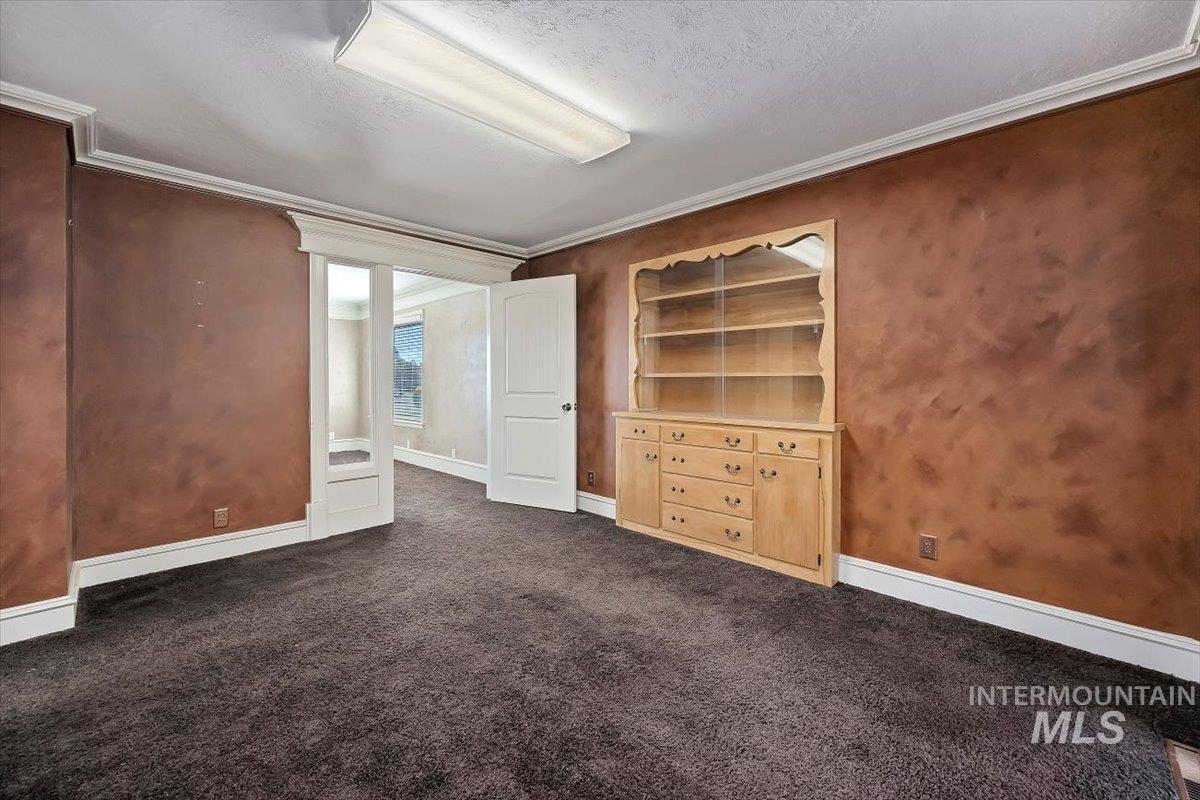 Unfurnished bedroom with ornamental molding, dark carpet, and a textured ceiling