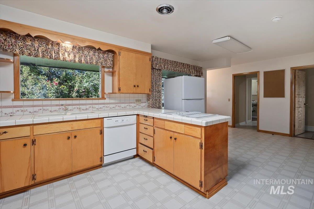 Kitchen with light floors, a peninsula, white appliances, and backsplash