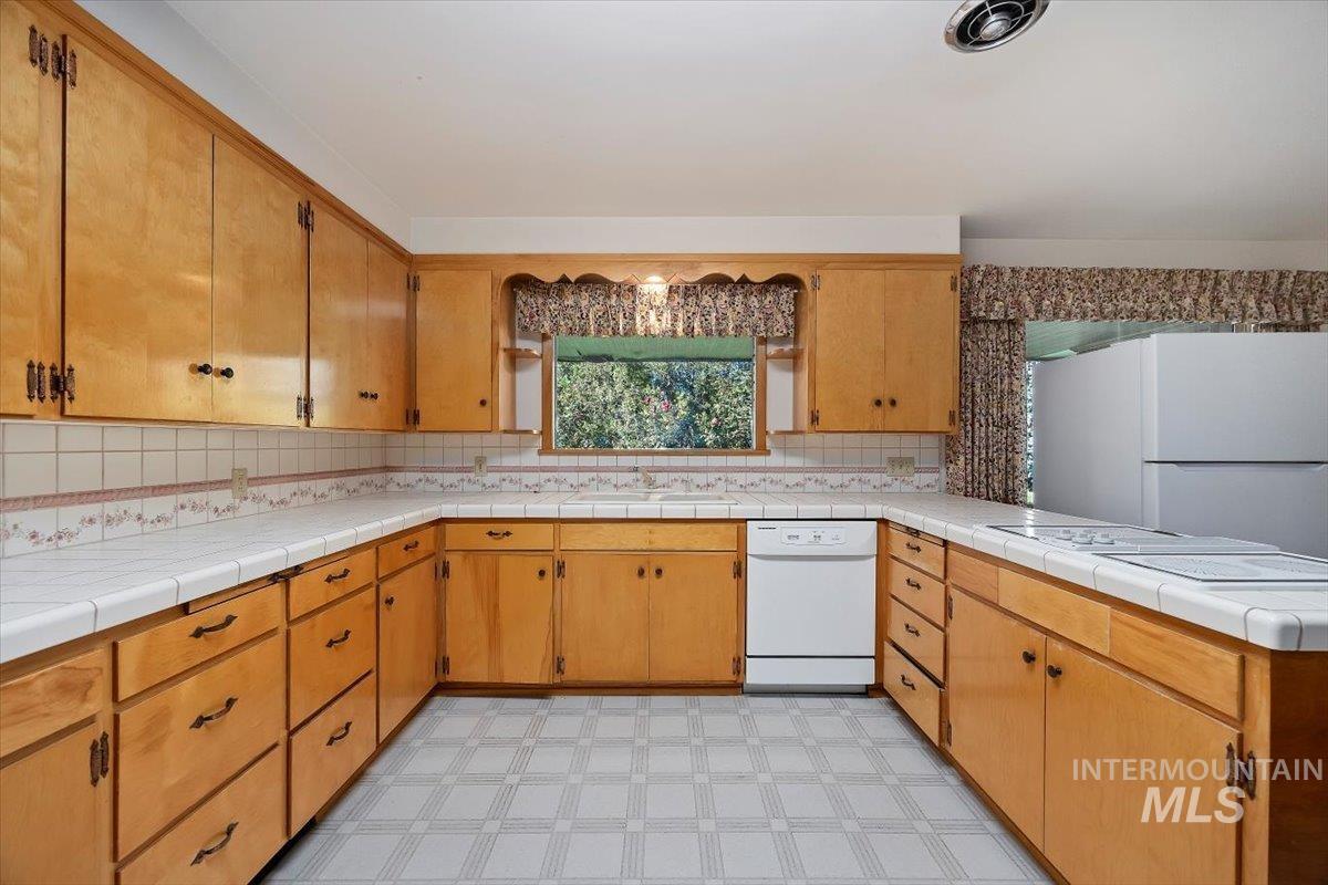 Kitchen featuring white appliances, a peninsula, light floors, and tile countertops