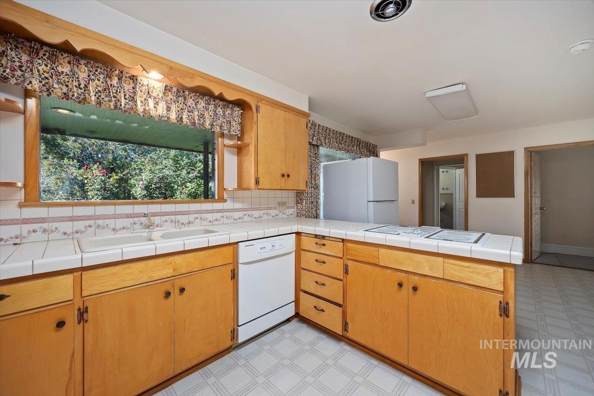 Kitchen with a peninsula, light flooring, white appliances, backsplash, and tile counters