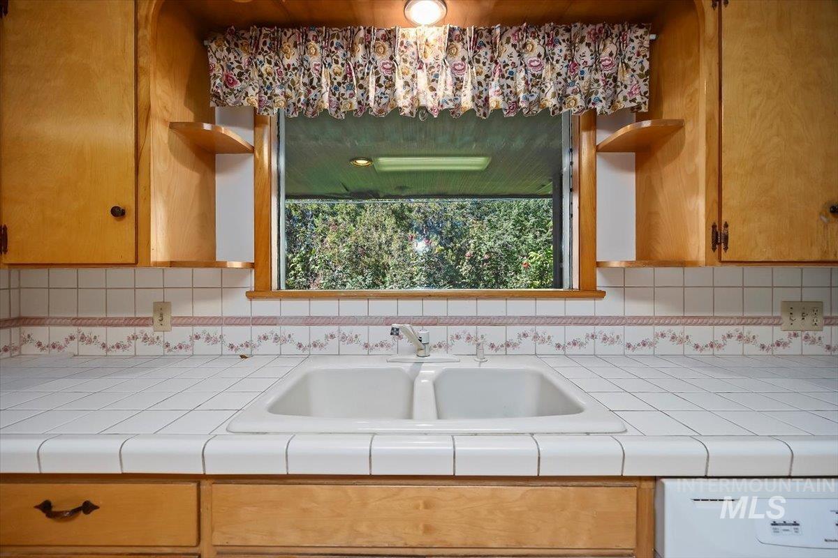 Kitchen featuring open shelves, dishwashing machine, tile countertops, and tasteful backsplash