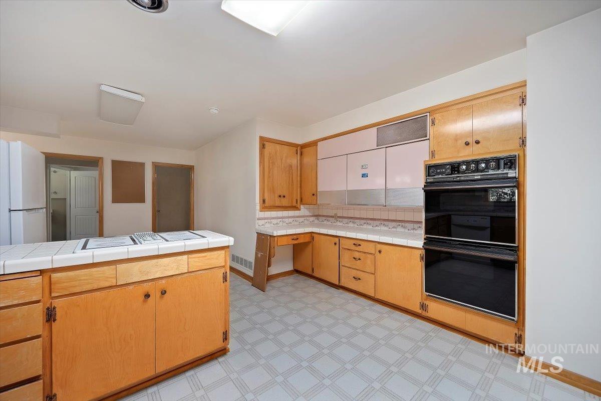 Kitchen featuring white appliances, light floors, tile countertops, light brown cabinets, and backsplash
