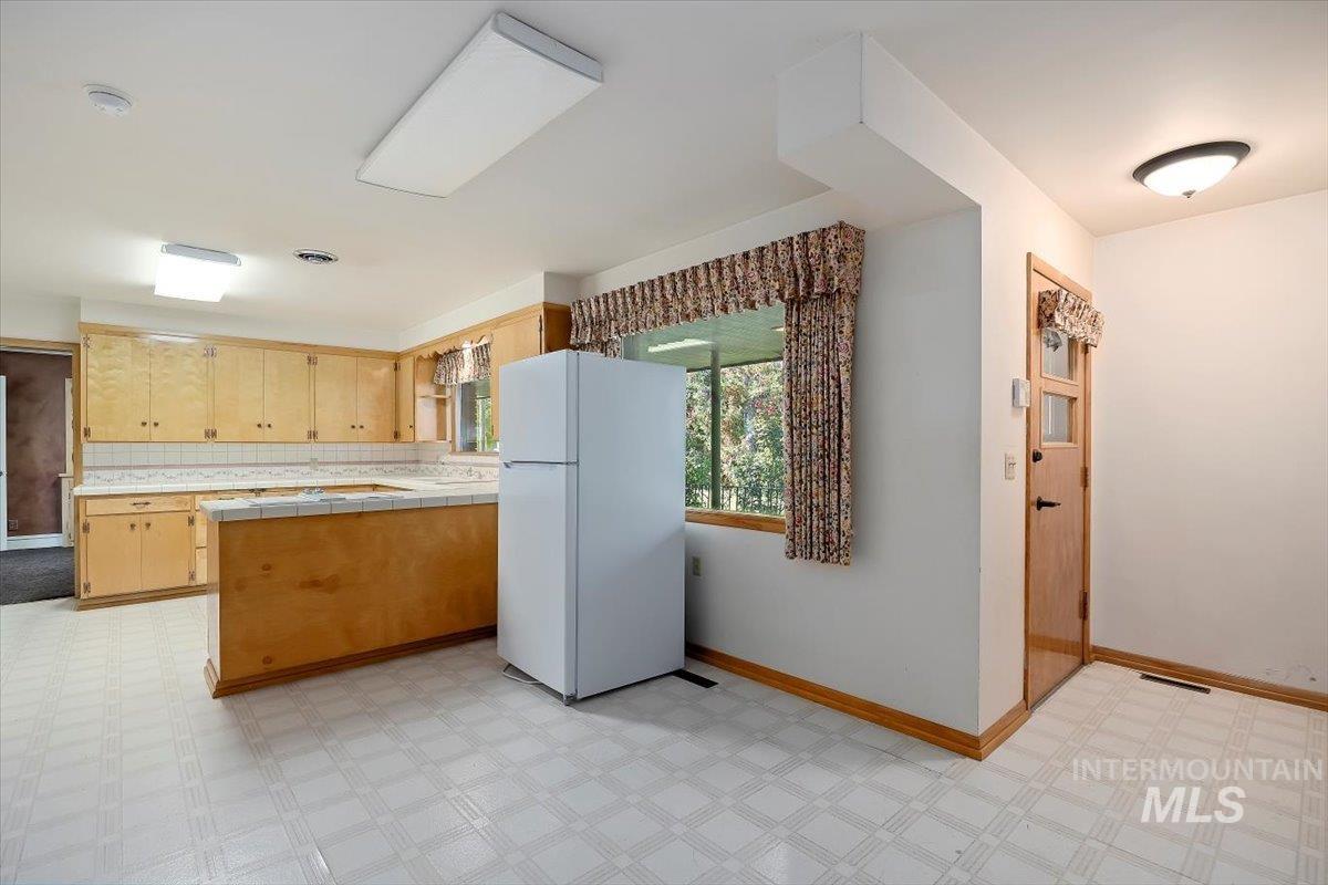 Kitchen featuring tile countertops, freestanding refrigerator, light flooring, and a peninsula