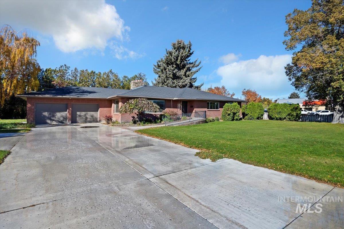 Single story home with a front yard, driveway, a garage, brick siding, and a chimney