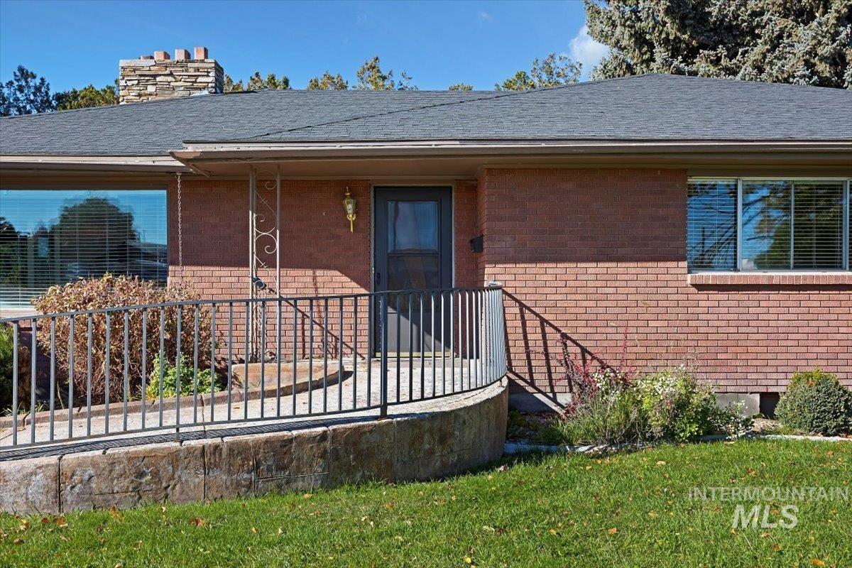 Entrance to property featuring brick siding, a chimney, a yard, and a shingled roof