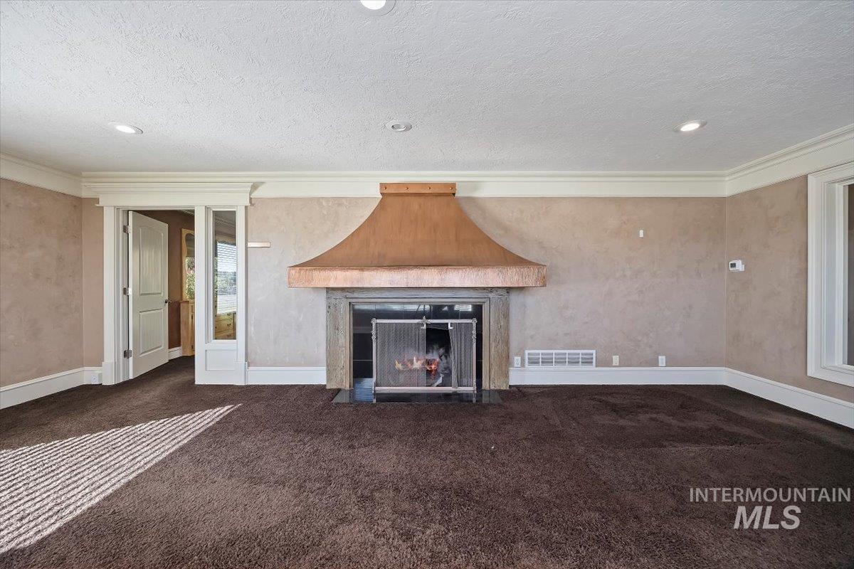 Unfurnished living room featuring a fireplace with flush hearth, a textured ceiling, dark carpet, crown molding, and recessed lighting
