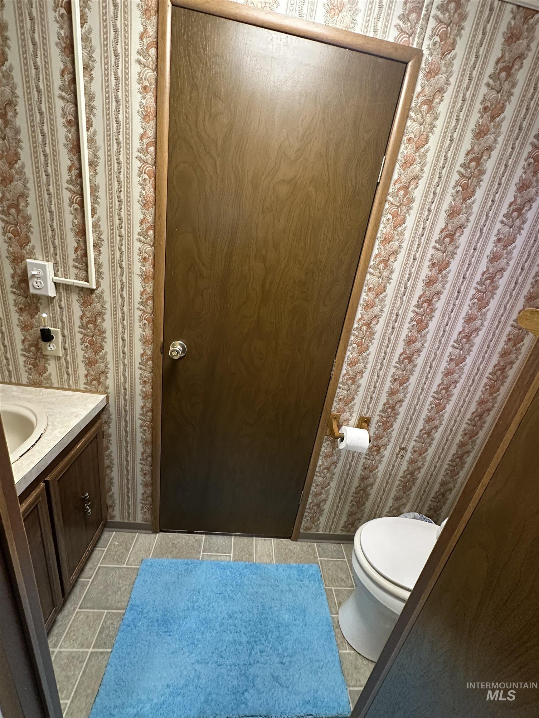 Bathroom with wallpapered walls, vanity, and light tile patterned floors