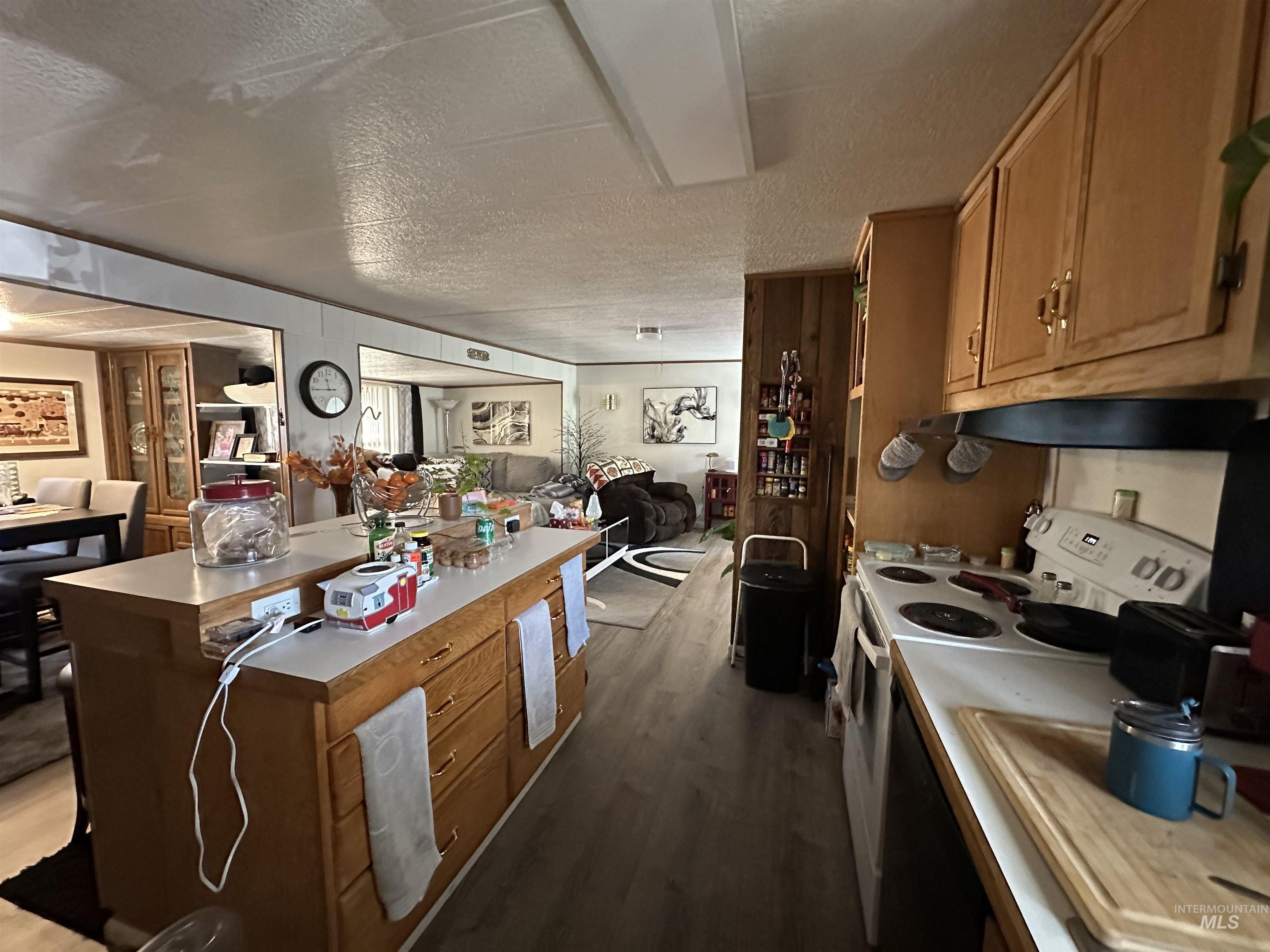 Kitchen with open floor plan, brown cabinetry, white range with electric stovetop, a textured ceiling, and dark wood-type flooring