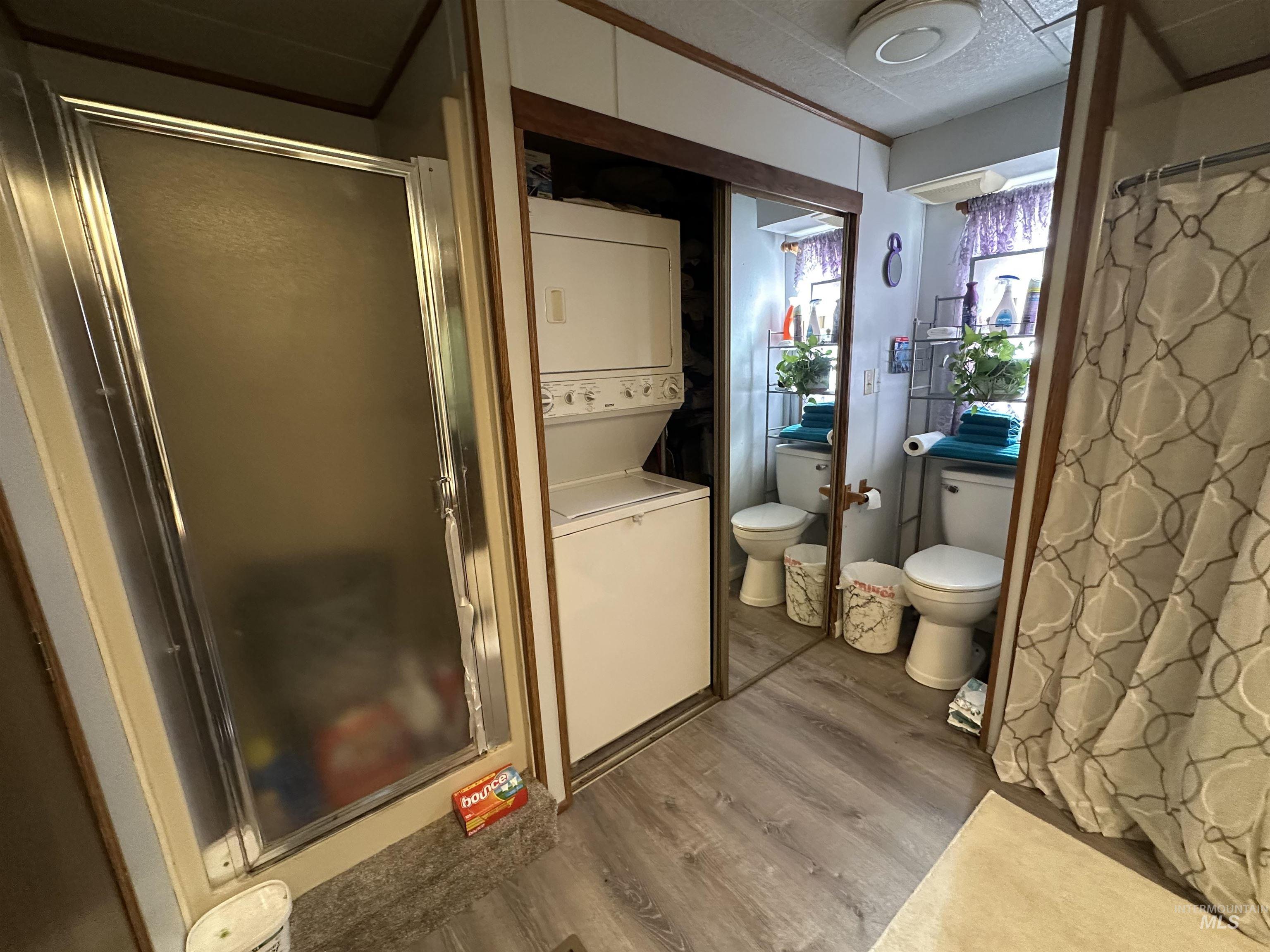 Bathroom with a shower stall, dark wood-style flooring, and stacked washer and clothes dryer