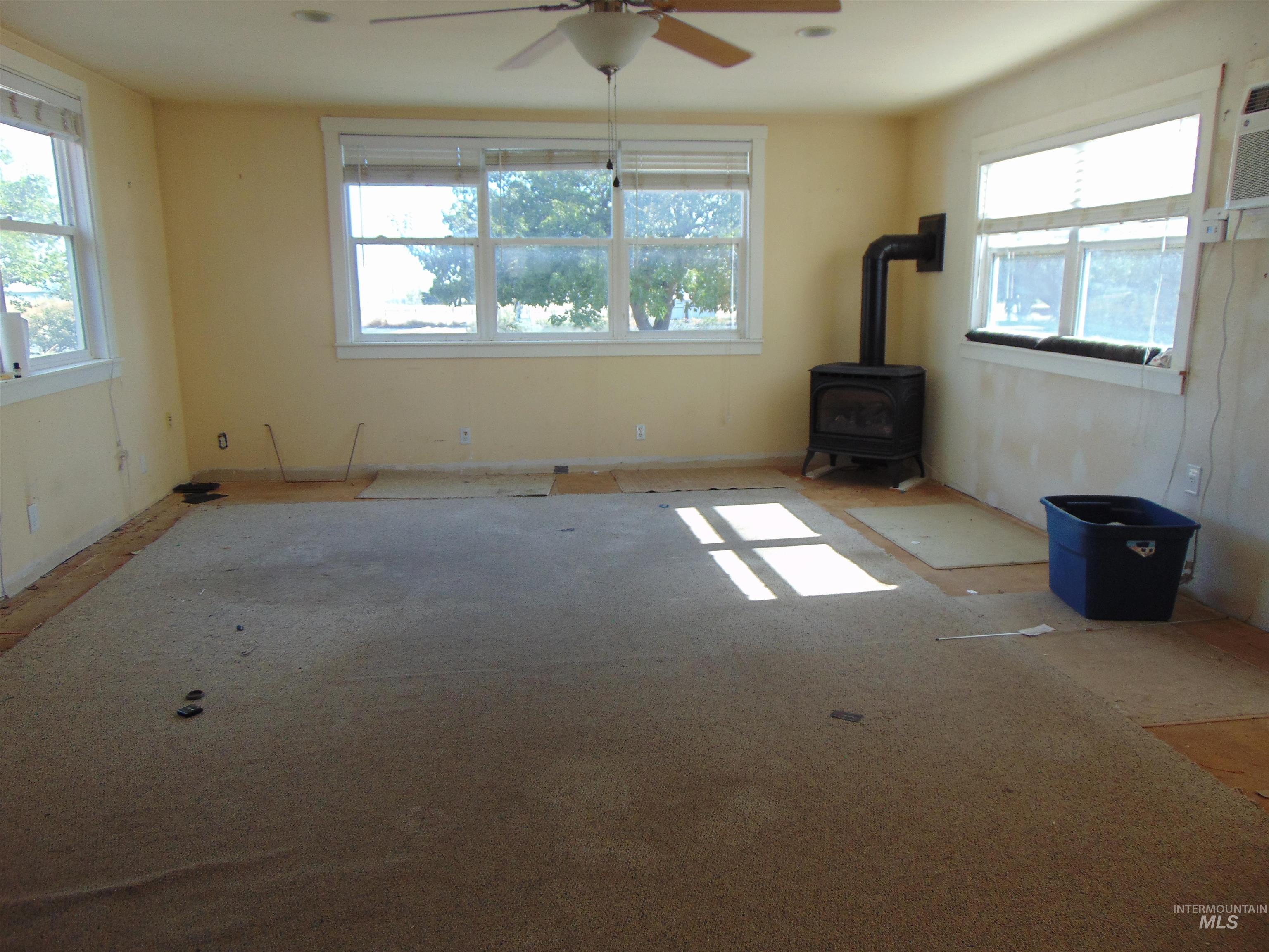 Unfurnished living room featuring a wood stove and a ceiling fan