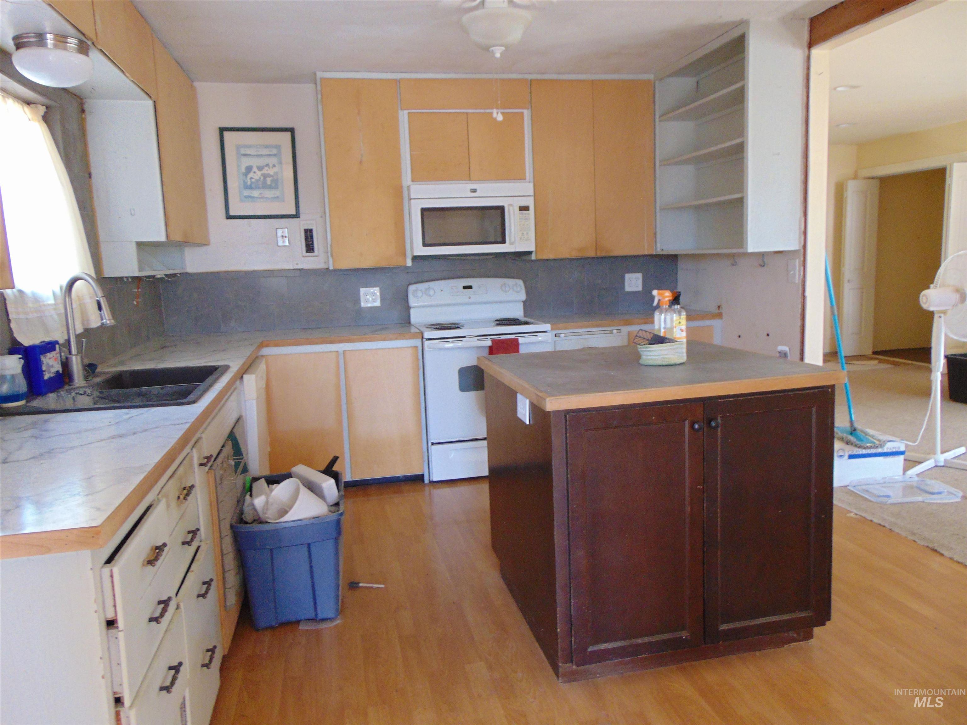 Kitchen with white appliances, light countertops, light wood-style floors, and a center island