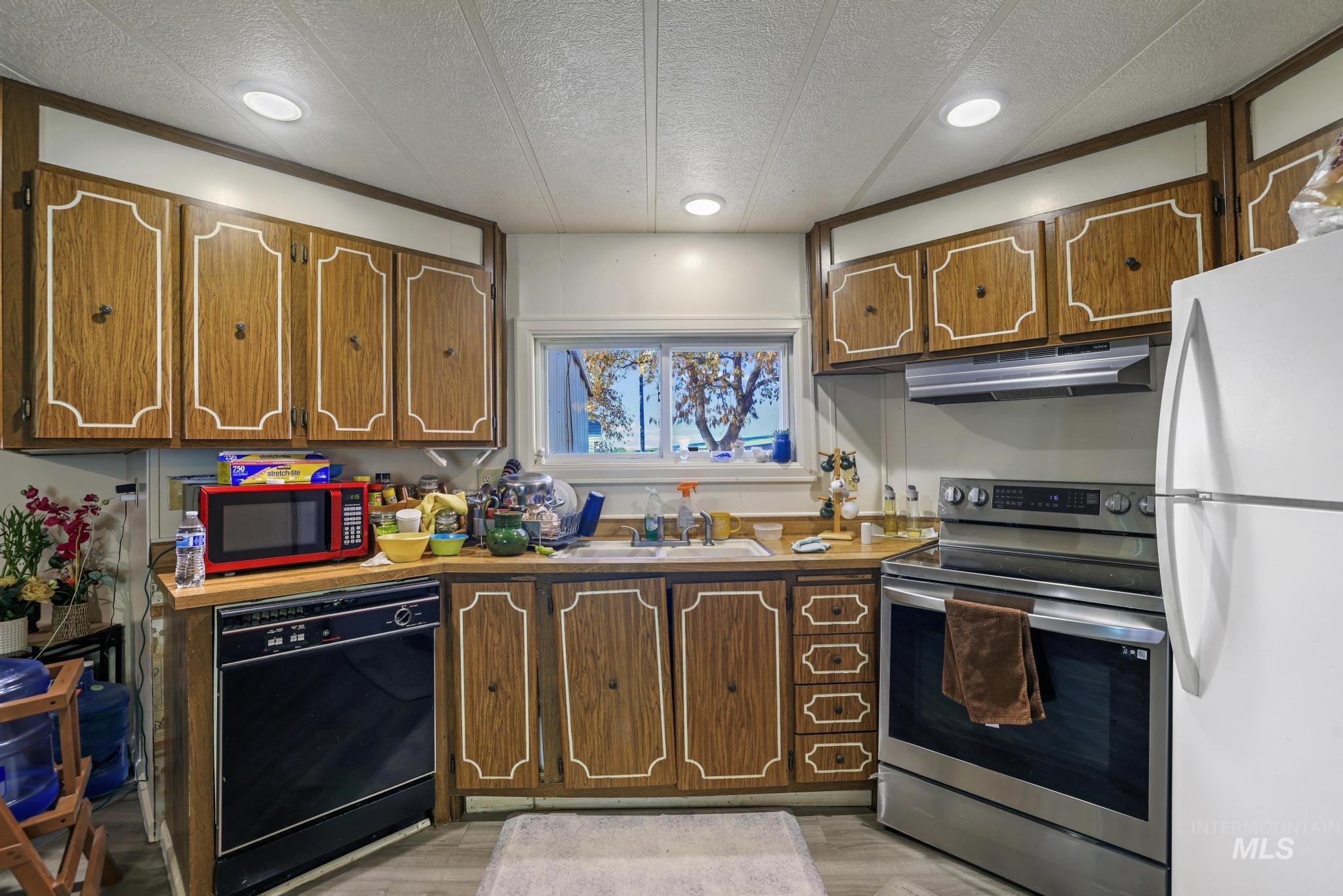 Kitchen with a textured ceiling, stainless steel range with electric stovetop, freestanding refrigerator, black dishwasher, and under cabinet range hood